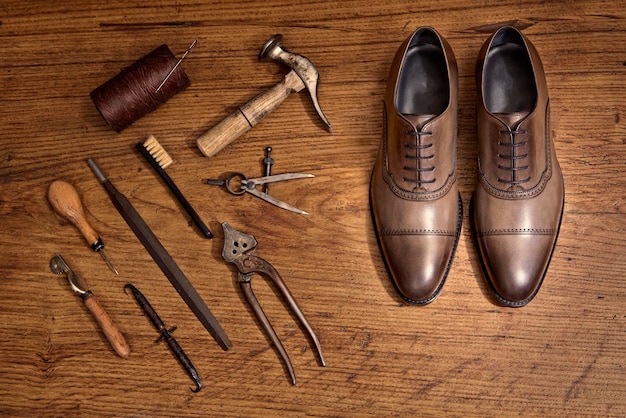 Handmade mens shoes and shoe making equipment on a wooden surface.