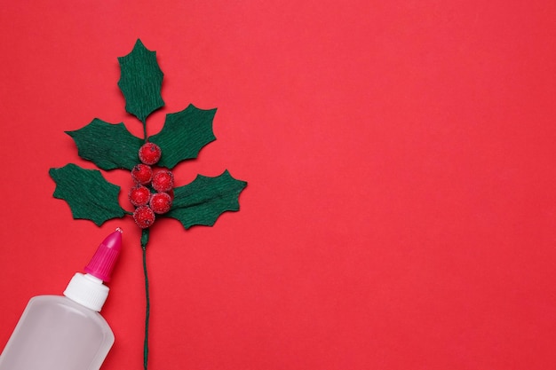 Handmade mistletoe branch and glue on red background flat lay Space for text