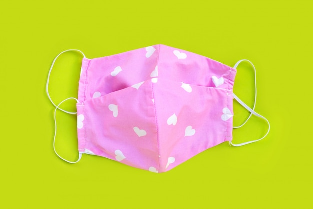 Handmade pink and heart shape cloth masks on green background.