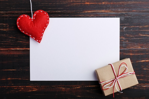 Handmade red felt heart and gift, next to white paper, on wooden table