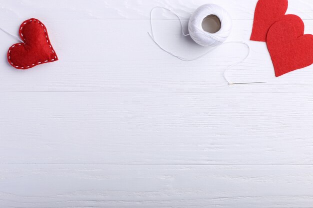 Handmade red felt heart next to threads and a needle on a white table. Women's Day Concept, Copy Space.