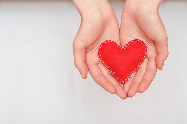 Handmade red heart in the hands of a girl on a white table with copy space. Valentine´s