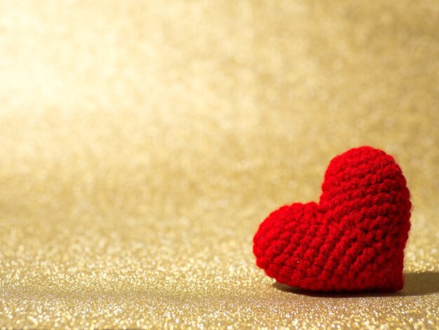 Handmade red yarn heart on gold abstract background.