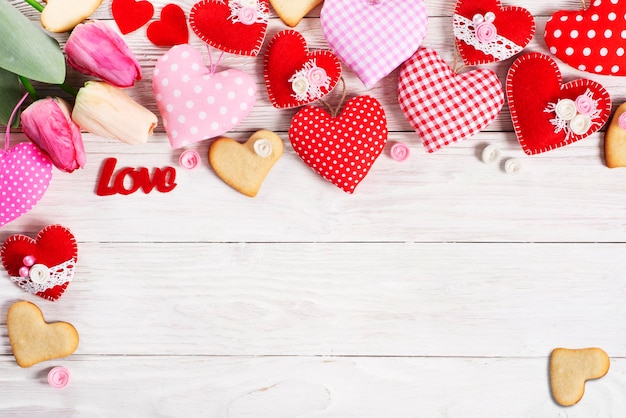 Handmade sewed Valentine fabric hearts with tulips and cookies flat lay background on white wooden table