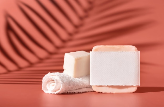 Handmade soap bars with blank label and small towel on pink close up palm leaf hard shadows