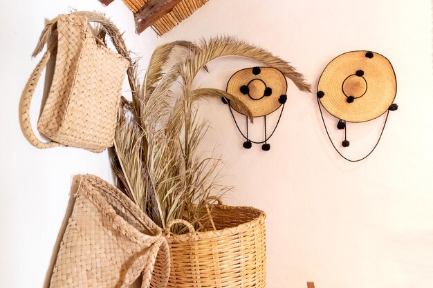 Handmade straw bags and straw hats hanging on a white wall.