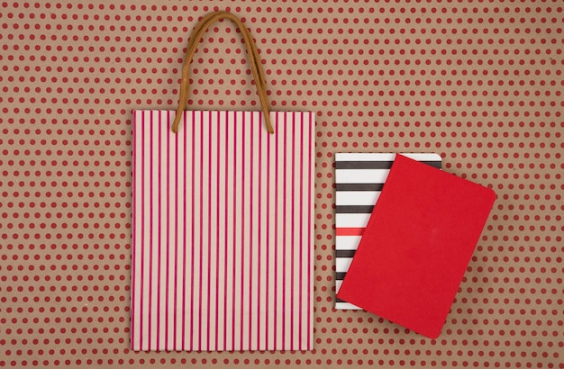 赤い水玉模様のクラフト紙の背景に手作りの縞模様のショッピングバッグギフトバッグとメモ帳