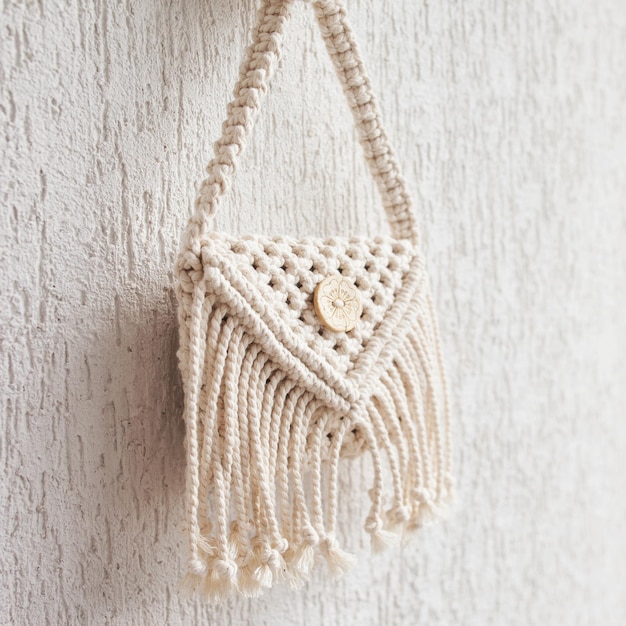 Handmade white macrame bag on the white wall, ECO friendly. Hobby knitting handmade macrame. Modern summer concept. Copy space
