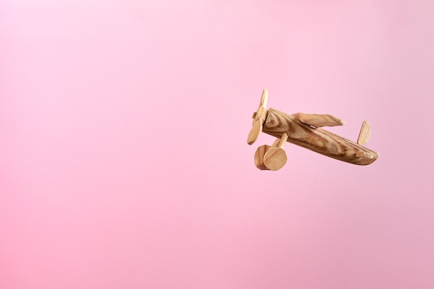 Handmade wooden airplane toy flying on a pastel pink background. Close up.