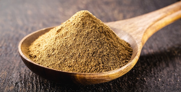 Handmade wooden spoon with cinnamon powder on brown wooden table, food close-up, food condiment powder.