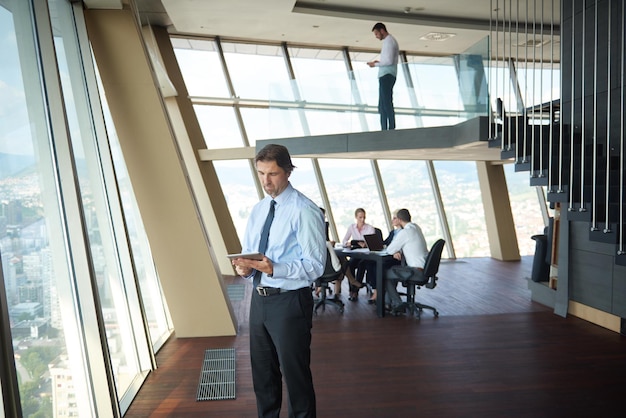 handosme business man working on tablet computer at modern bright office indoors with his team in group working together in background