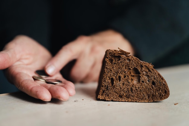 Photo a handout of bread for the poor the concept of poverty and hunger hands of senior woman with bread and coins on wooden background poverty concept