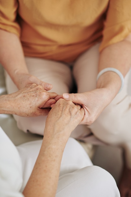 Hands of adult daughter holding hands of her senior mother