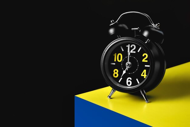 The hands of the alarm clock indicate seven o39clock A black alarm clock stands on the corner of a yellowblue cube