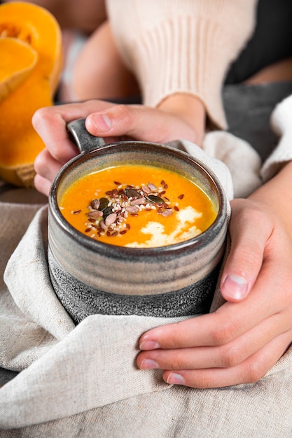 Фото Руки держат чашку домашнего тыквенного супа с семенами кунжута и семенами льна крупным планом в тепле