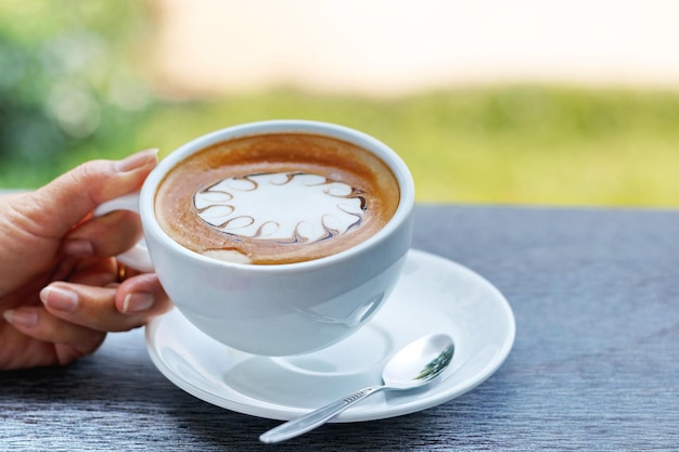 Hands are holding a cup of hot latte coffee on a natural blurred background