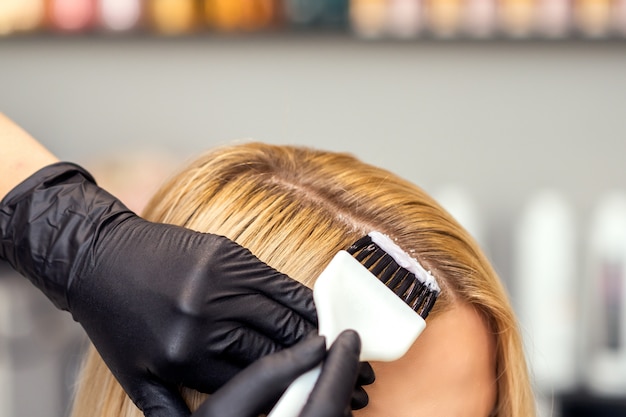 Hands are painting the female hair in a white color close up.