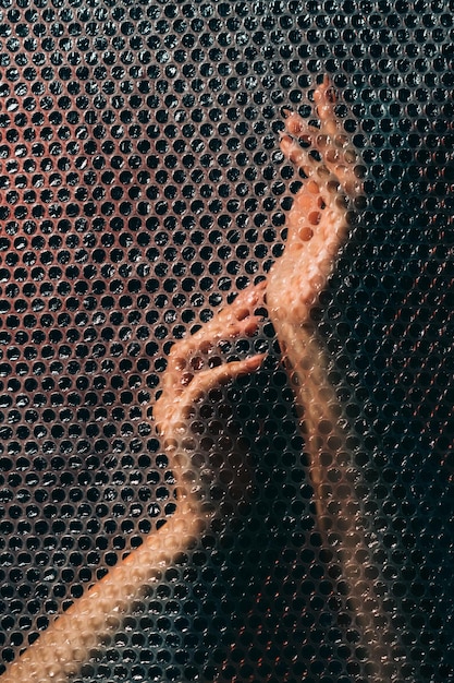 Hands art. Graceful performance. Spiritual practice. Freedom tranquility. Gentle sensual female arms behind transparent plastic bubble wrap texture wall in darkness.