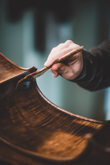 Photo hands of artisan luthier varnishing, building a double bass