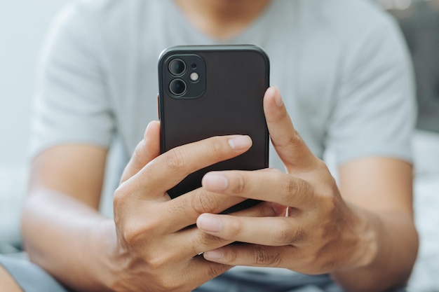 Photo hands of asian man holding checking touching scrolling smartphone from bed room