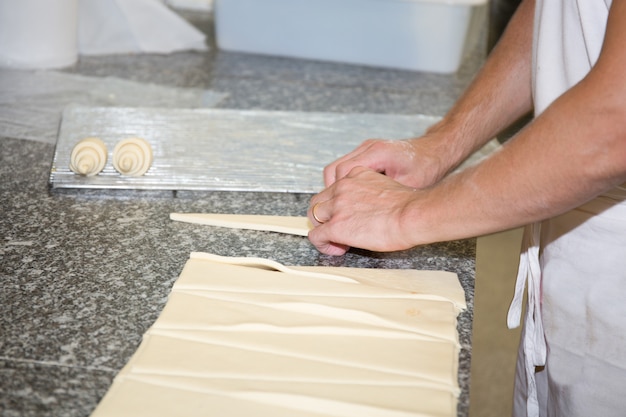 Hands of a baker making croissants on grey background