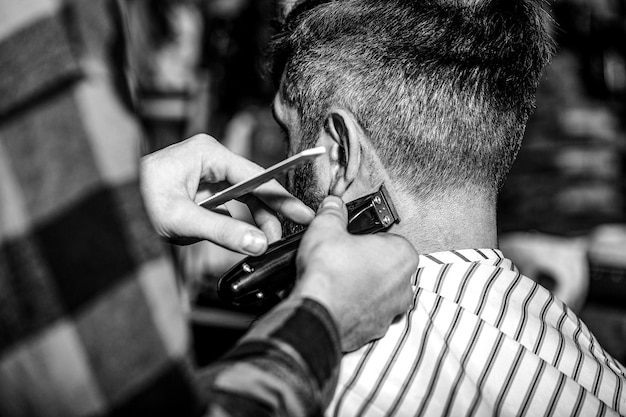 Hands of barber with hair clipper close up Haircut concept Hipster client getting haircut Black and white