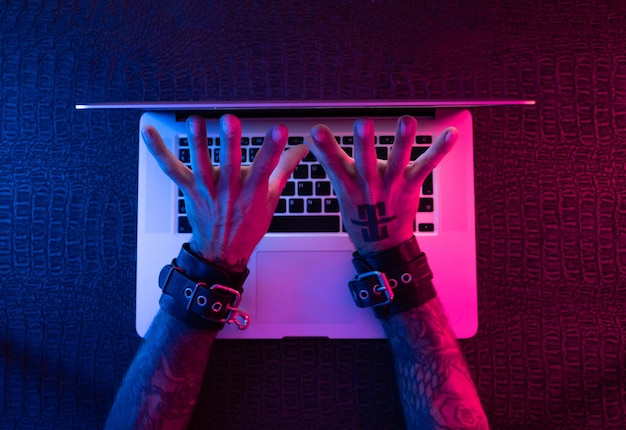 Hands in bdsm handcuffs with a laptop in neon light