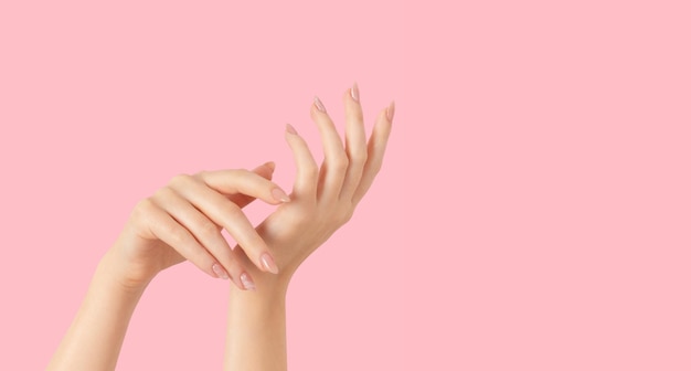 Hands of a beautiful wellgroomed beige nude marble design nails gel polish on a pink background