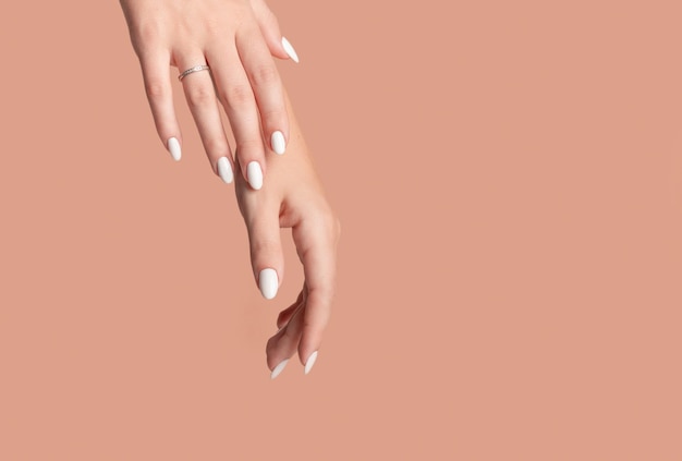 Hands of a beautiful wellgroomed woman with feminine nails on a beige background Manicure