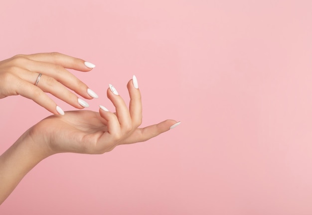 Hands of a beautiful wellgroomed woman with feminine nails on a pink background Manicure