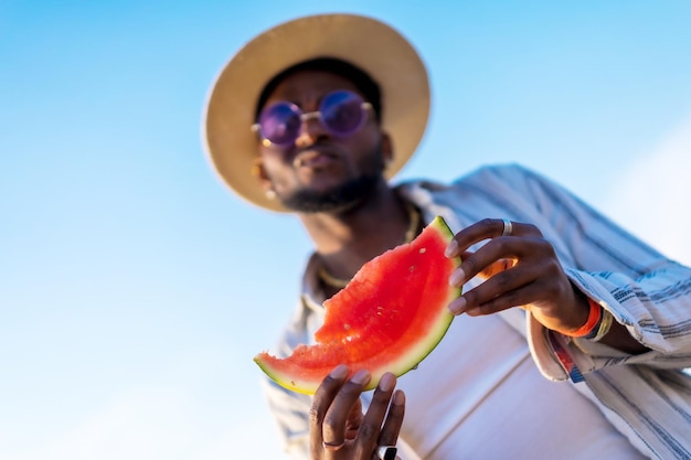 Hands of a black ethnic man enjoy the summer vacation on the beach eating a watermelon