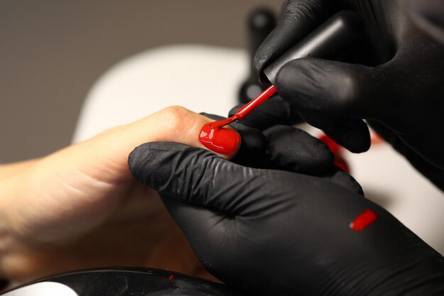 Hands in black gloves apply red varnish