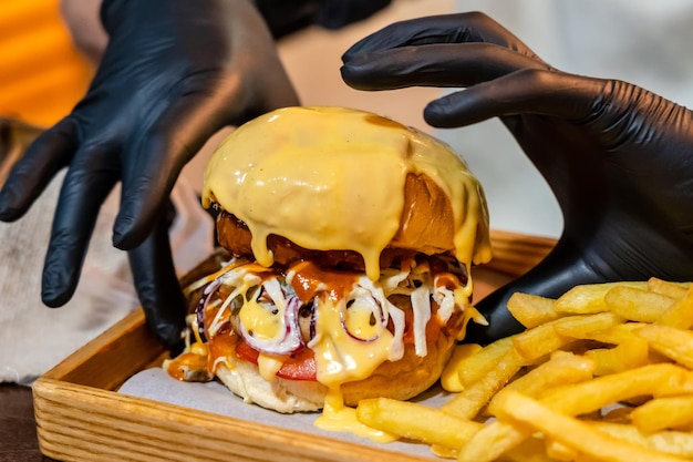 Hands in black gloves holding tasty burger with french fries