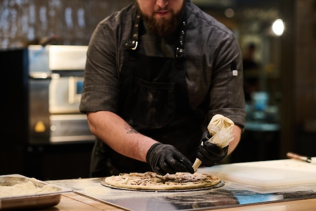 Hands in black gloves of young chef squeezing mixture of ingredients