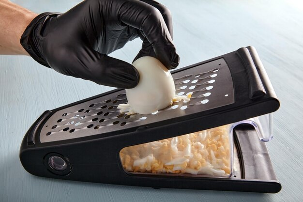 Hands in black latex gloves rub a hardboiled chicken egg on a metal grater on a wooden countertop