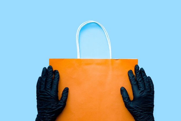 Hands in black surgical glove holding paper bag. Home delivery precaution measures against COVID-19, paper bag delivered without direct contact.