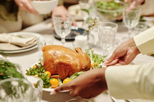 Hands of black woman putting plate with roasted poultry on dinner table