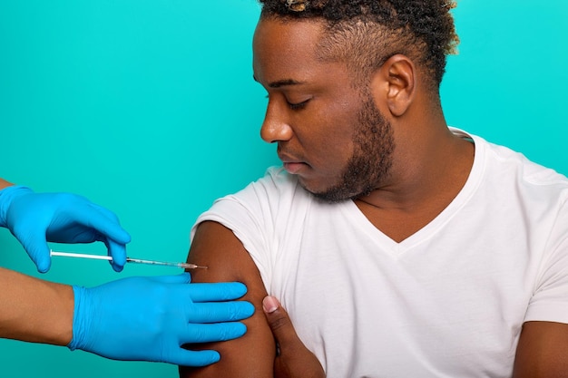 Hands in blue gloves inject the vaccine against the covid19 coronavirus using a syringe with the vaccine into the arm muscle of an AfricanAmerican man for immunization against the coronavirus