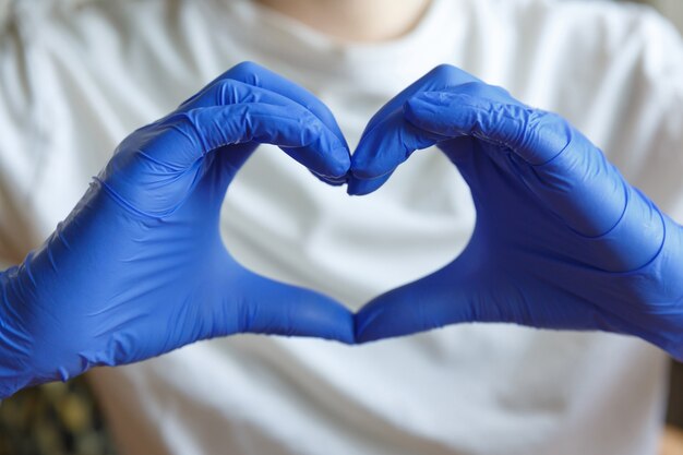 Foto le mani in guanti medici blu tengono le dita a forma di cuore. gesti con le mani.