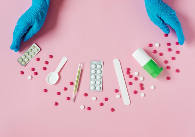 Hands in blue medical gloves Medical equipment on the pink background Blisters pills throat spray thermometer Medical concept flat lay