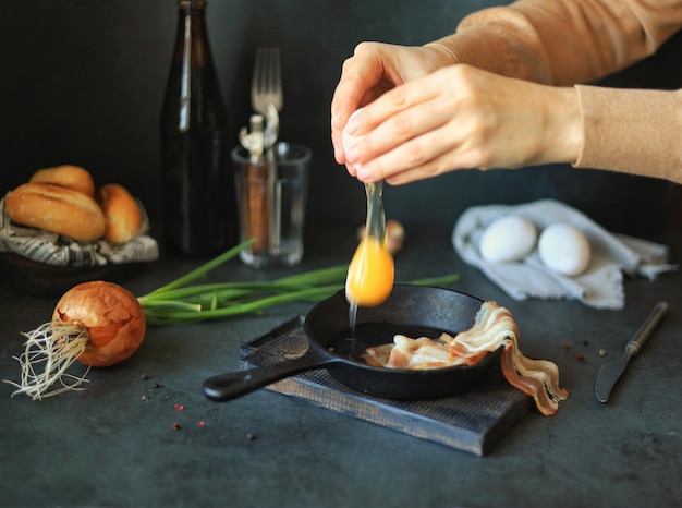 Hands break an egg over a frying pan on the kitchen table at home Cooking scrambled eggs and bacon