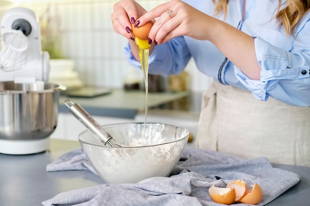 Hands break an egg into a bowl of flour