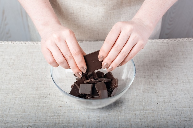 Hands breaking a bar of chocolate into small pieces in a glass bowl