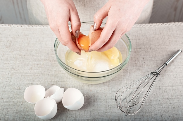 Hands breaking an egg over a glass bowl of sugar