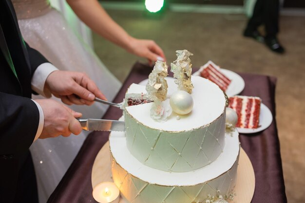 Hands of bride and groom cut of a slice of a wedding cake