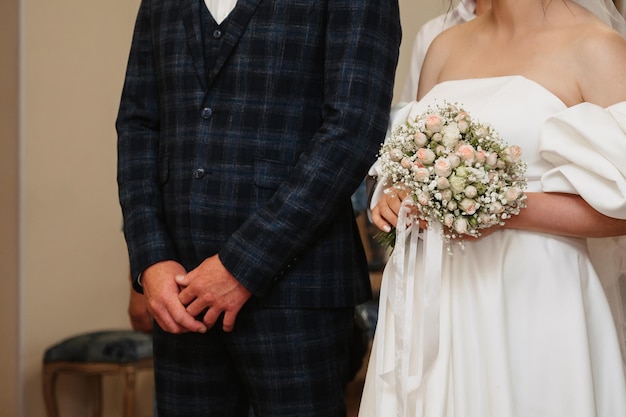 Mani della sposa e dello sposo con un bouquet nella sala cerimoniale il giorno del matrimonio