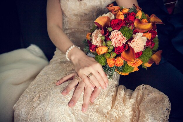 Руки жениха и невесты со свадебным букетом и кольцами на коленях невесты