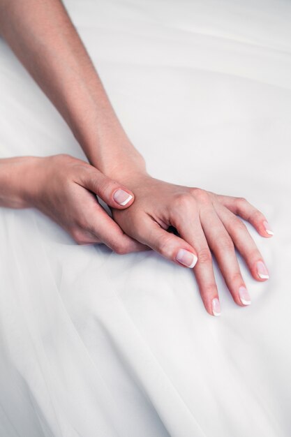 Hands of the bride with french manicure lay on a white cloth