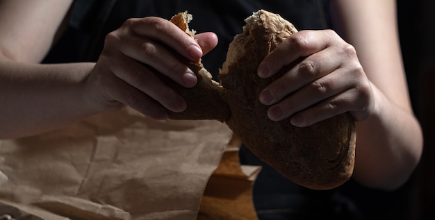 Руки ломали аппетитный свежий хлеб, вынутый из бумажного пакета. темный фон.