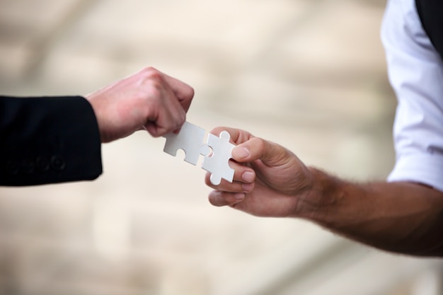 Hands of business people hold paper jigsaw puzzle and solving puzzle together